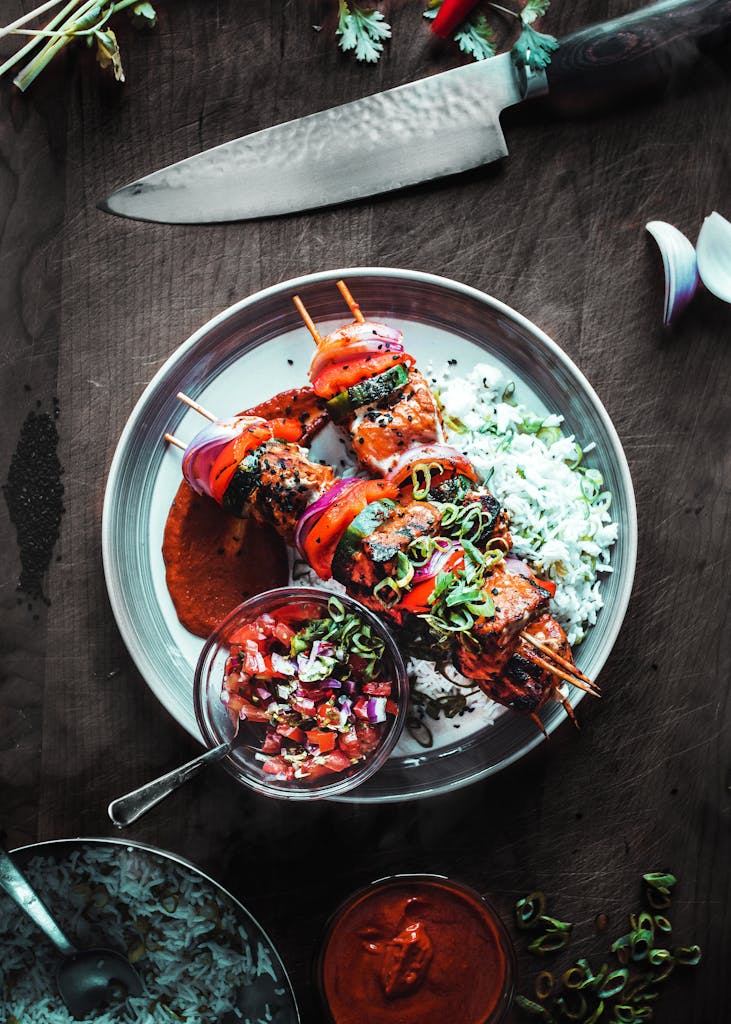 Delicious grilled skewers with rice and salsa served on a wooden table.